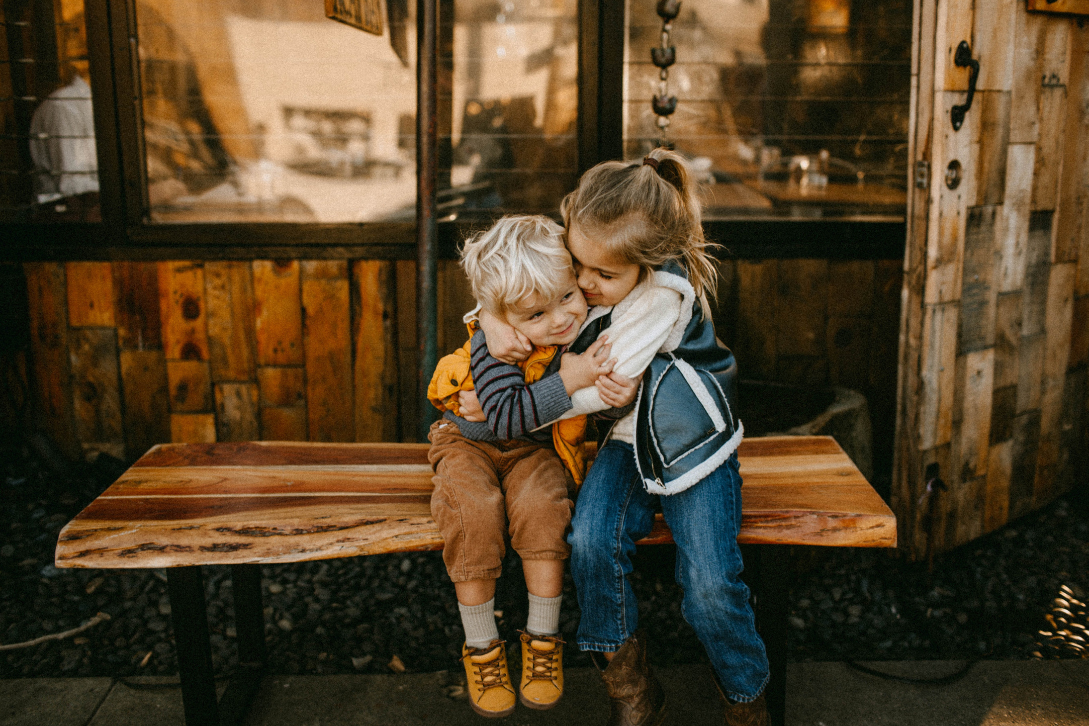 Children Seated on a Wooden Bench Hugging Each Other